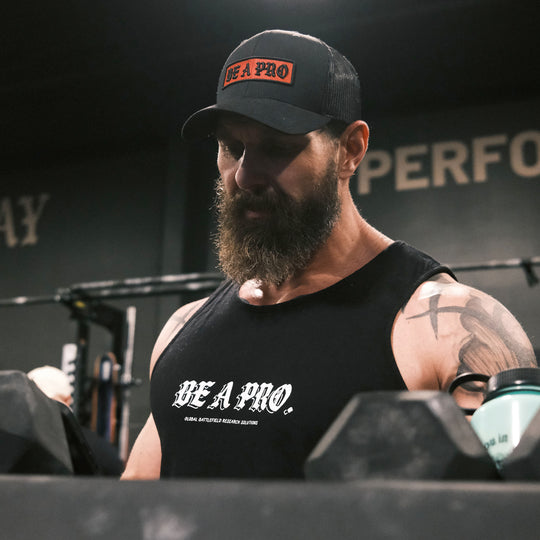 GBRS Group Old English Outline Be A Pro Tank.Global Battlefield Research Solutions in small print underneath.  Lifestyle setting in a gym. Be A Pro - A mindset to elevate your performance, keep you focused, and help spark motivation in others to foster the same mentality.