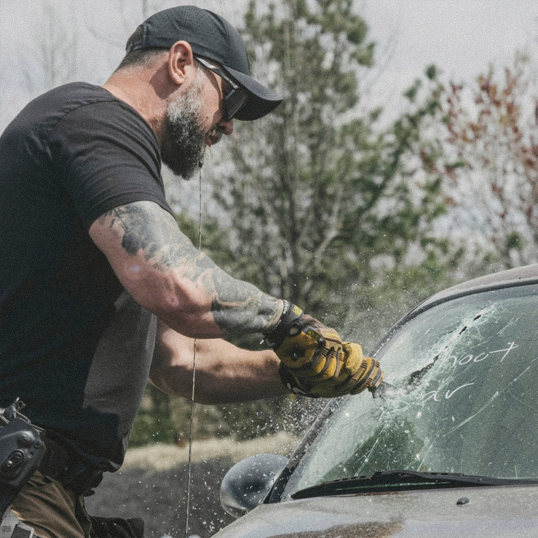 Man cutting open a car windshield with a black metal tool bar outdoors.