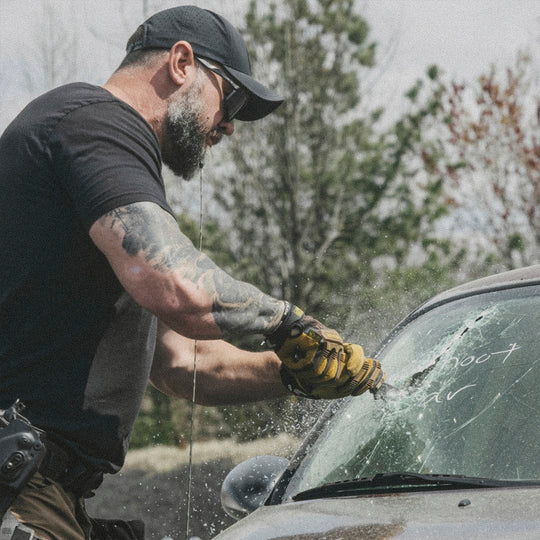 Man cutting open a car windshield with a black metal tool bar outdoors.