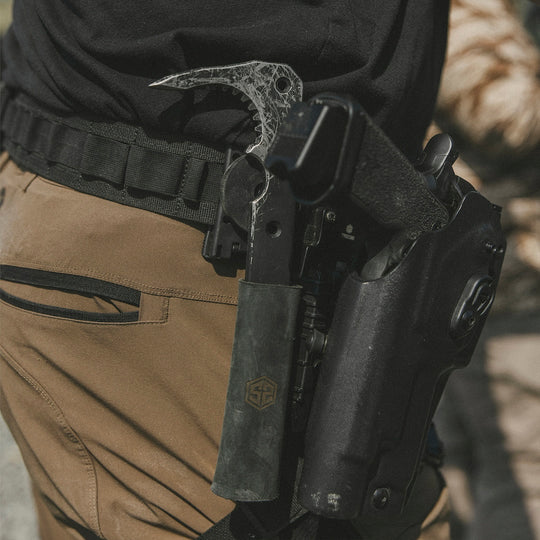 Person wearing pants with a tactical belt, holding a black metal tool bar and a holster holding a firearm.