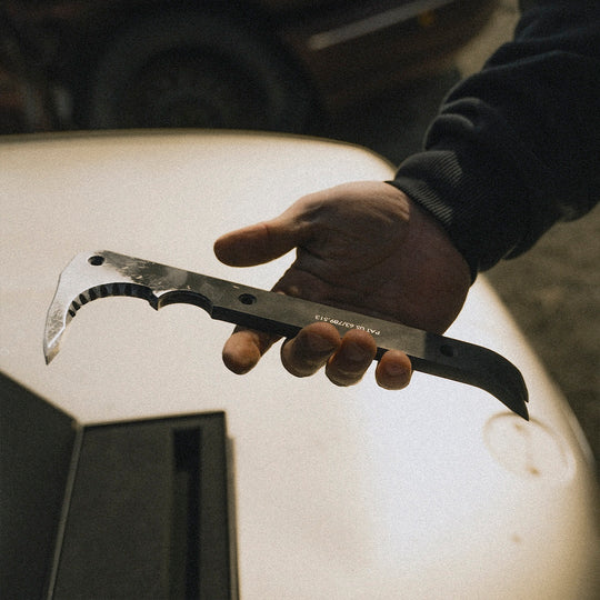 Hand holding a black metal tool bar with a car blurred in the background.