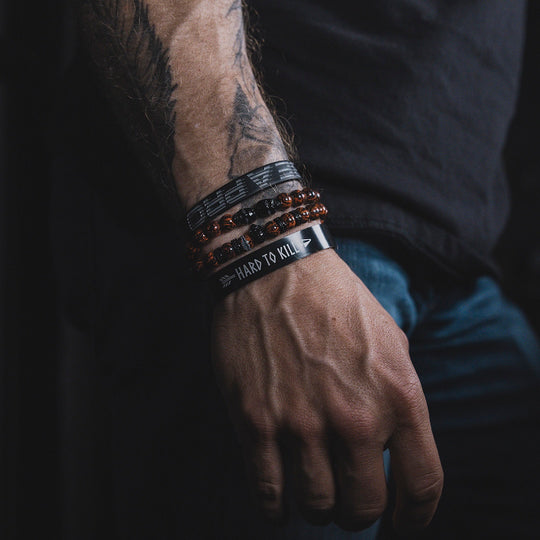 Man wearing GBRS Group Hard to Kill Cuff on wrist among other bracelets and accessories, with his arm resting at his side
