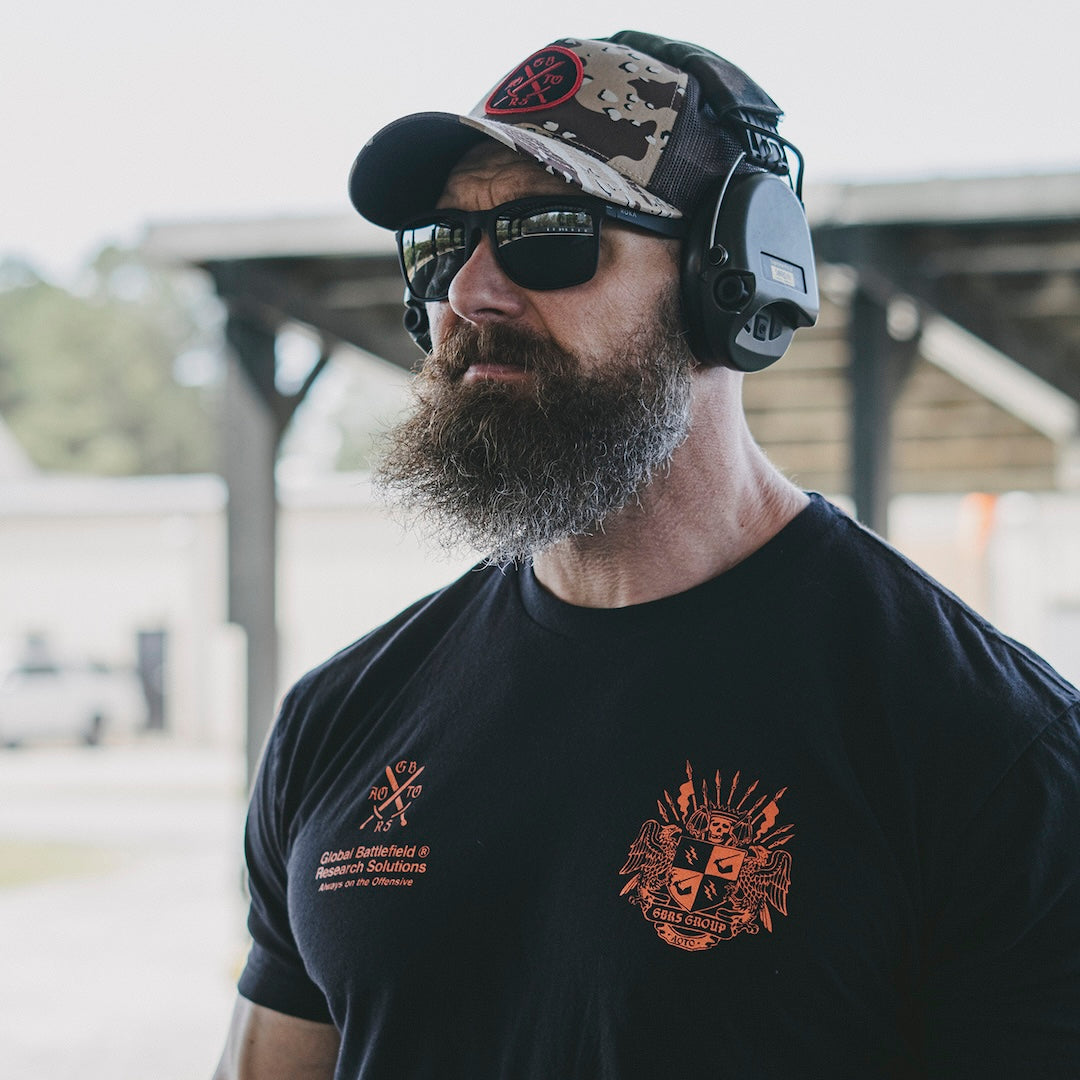 Man wearing a black t-shirt with a GBRS Group design, sunglasses, and a hat outdoors.