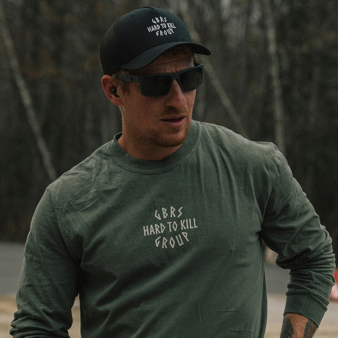 Model wearing the GBRS Group Hard to Kill Long Sleeve, Trucker Hat, and sunglasses outdoors