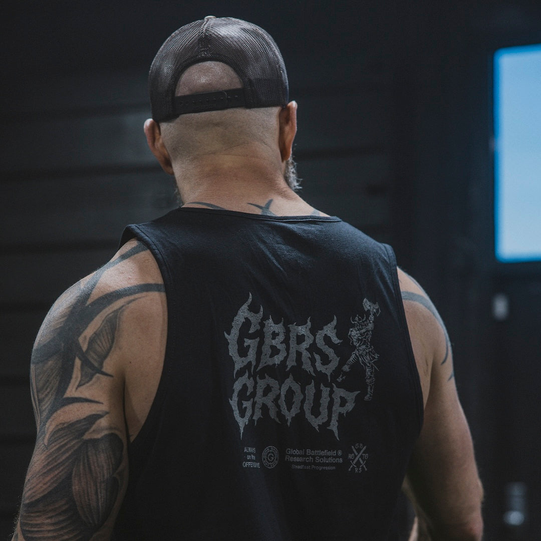 Man wearing a black tank top with 'GBRS GROUP' text, standing in a gym setting.