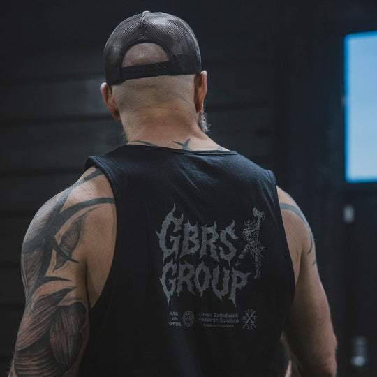 Man wearing a black tank top with 'GBRS GROUP' text, standing in a gym setting.