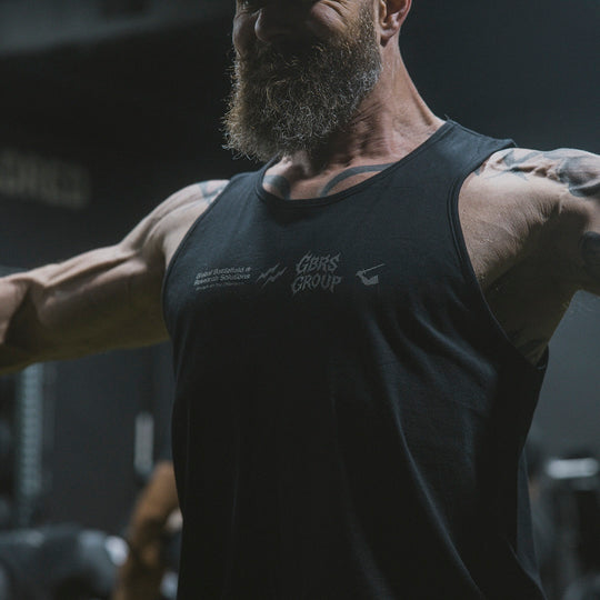 Man with tattoos and a beard wearing a black tank top in a gym setting