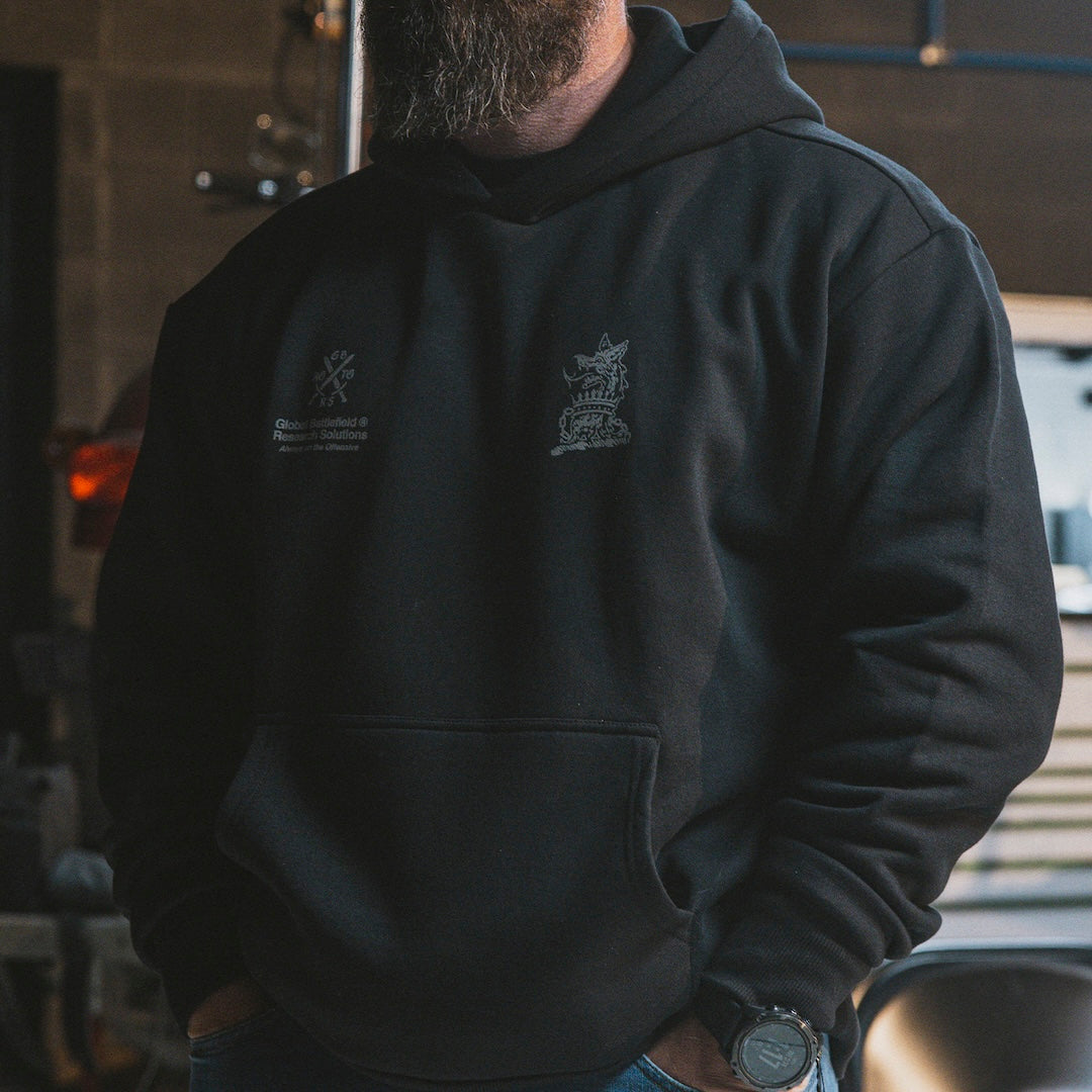 Person wearing a black hoodie with logos on the front, standing in an industrial setting.