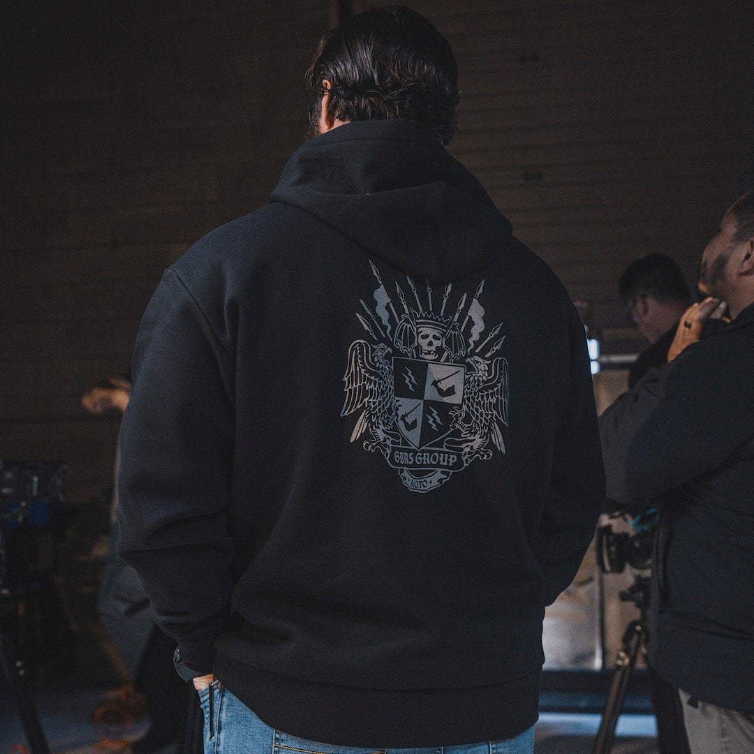 Person wearing a black hoodie with a GBRS Group design on the back, standing in a dimly lit room.