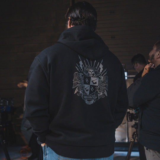 Person wearing a black hoodie with a GBRS Group design on the back, standing in a dimly lit room.