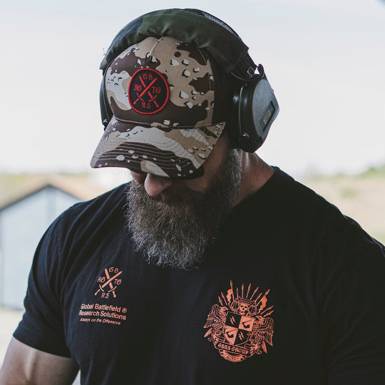 Man wearing a black t-shirt and a camouflage cap with an embroidered patch in the middle