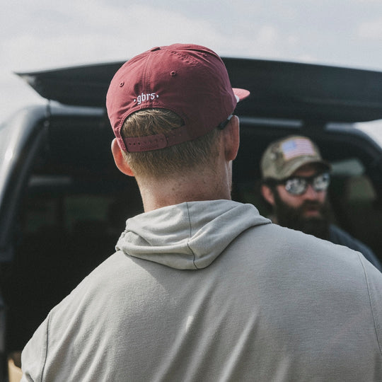 Two men standing next to a car, one wearing a red cap with 'gbrs' branding in white.