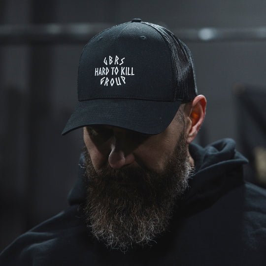 Man wearing GBRS Hard to Kill Trucker Hat in a gym setting