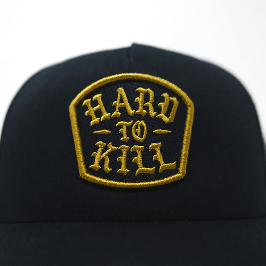 GBRS Group Hard To Kill Trucker Hat. Richardson 112FP with Classic Trucker vibes. Close up of gold embroidery