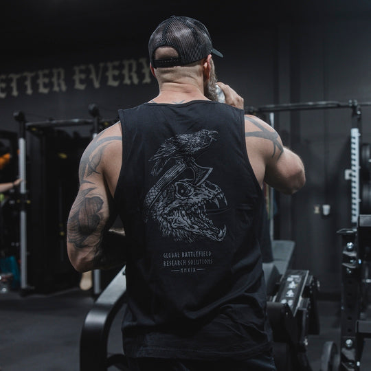 Man wearing GBRS Hard to Kill Axe and Talon Tank in a gym and drinking water, showing the back design