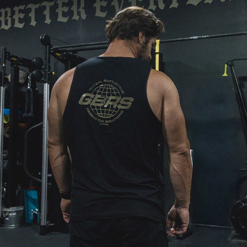 A man viewed from behind in a gym, wearing the GBRS Group Bravado Tank with a large graphic design visible on the back.
