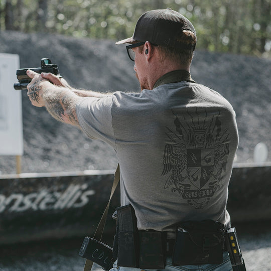 Man in tactical gear aiming a handgun at an outdoor shooting range.