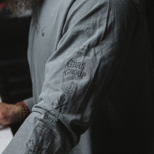 Close up of a gray long sleeve shirt with visible branding and text on the arm's side