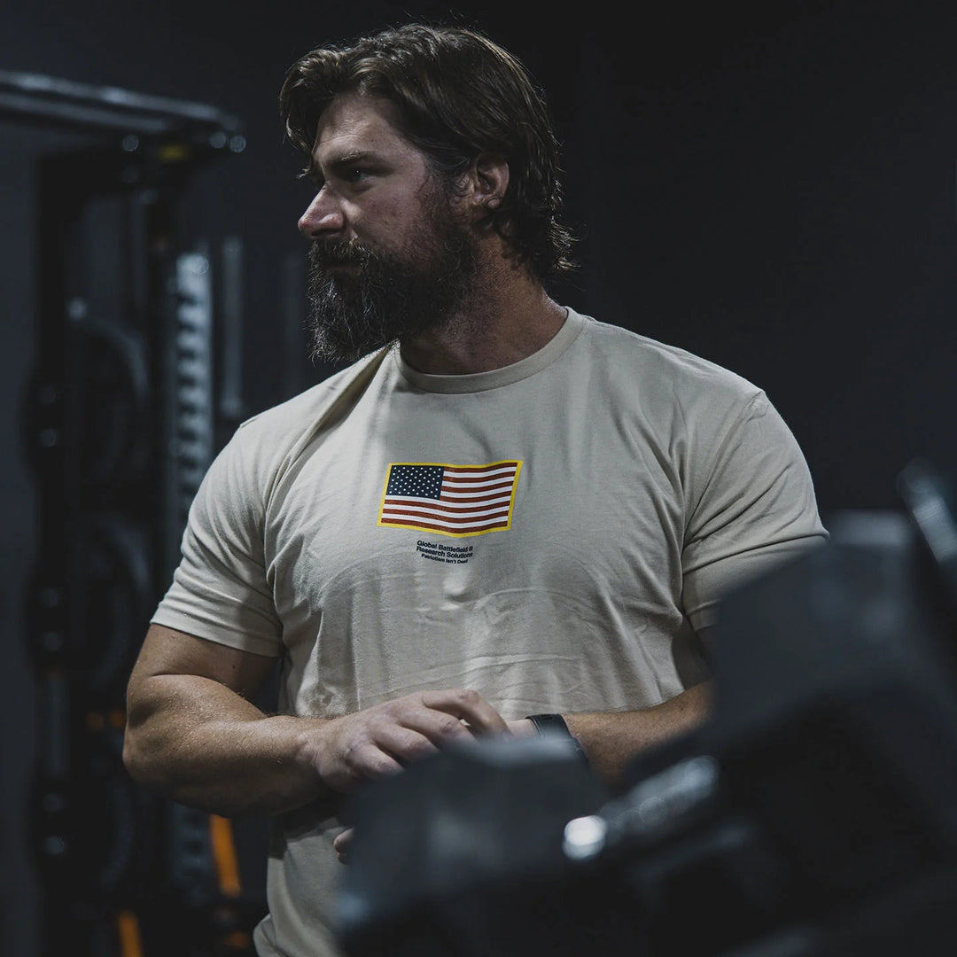 Man wearing the GBRS Group Front and Center Cream Short Sleeve Shirt with an American flag design in the center, while in a gym setting