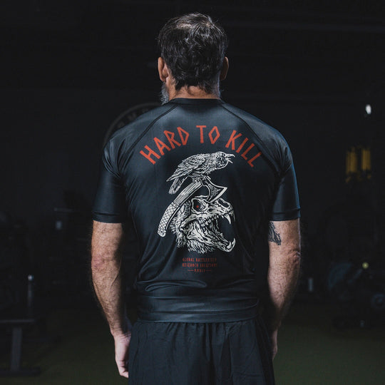 Image of a man wearing the GBRS Group Hard to Kill Rash Guard in a gym setting showing the design on the back