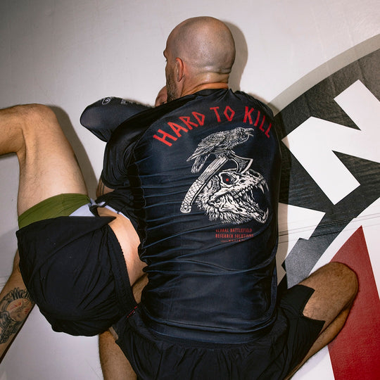 2 men engaging in Brazilian Jiu Jitsu in a gym setting showing the design on the back of the GBRS Group Hard to Kill Rash Guard