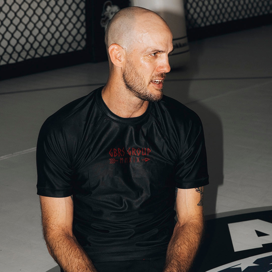 Man wearing the GBRS Group Hard to Kill Rash Guard while sitting up right and looking to the right 