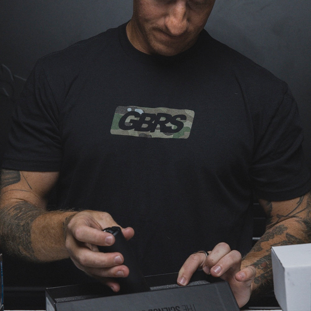 Person wearing the GBRS Group Infiltration Short Sleeve Shirt in black, while inside a storage room and packing a box.