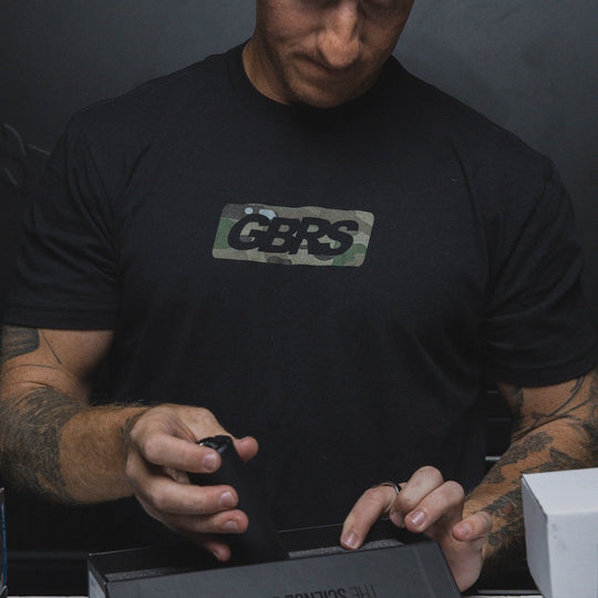 Person wearing the GBRS Group Infiltration Short Sleeve Shirt in black, while inside a storage room and packing a box.