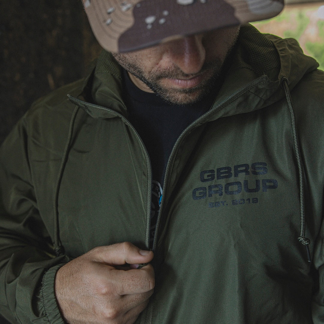 Man unzipping a green GBRS Group Instructor Windbreaker Jacket