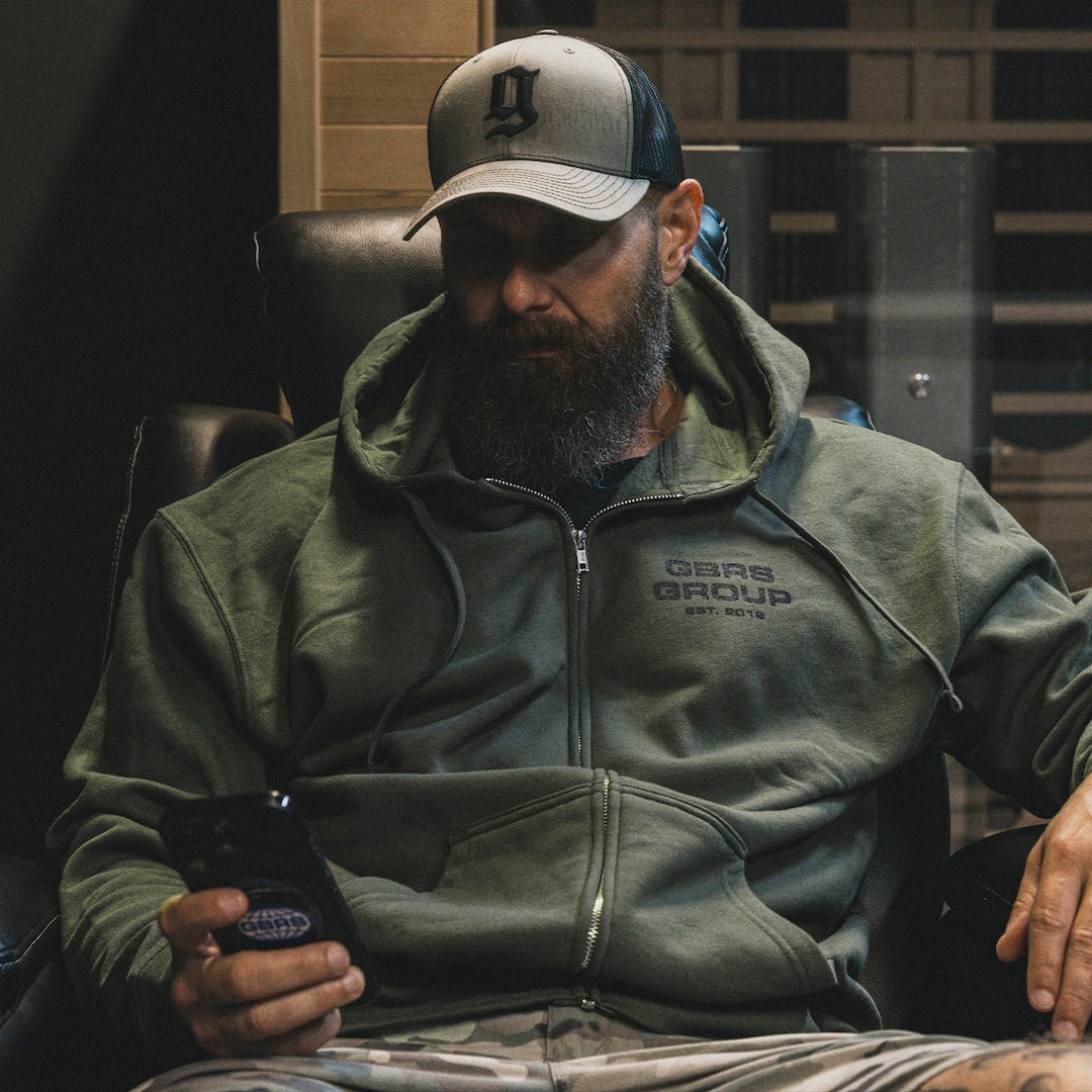 Person sitting down and looking at their phone, wearing the GBRS Group Instructor Zip Up Hoodie