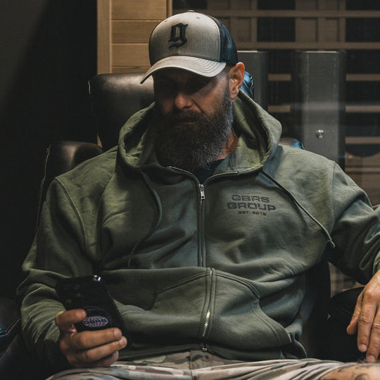 Person sitting down and looking at their phone, wearing the GBRS Group Instructor Zip Up Hoodie