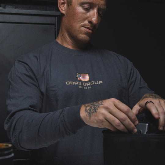 Man wearing the graphite GBRS Group International Long Sleeve Shirt while packing a bag