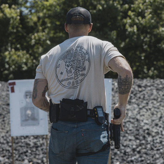 Man wearing the GBRS Group Lady Liberty Short Sleeve Shirt, holding a firearm at an outdoor range.