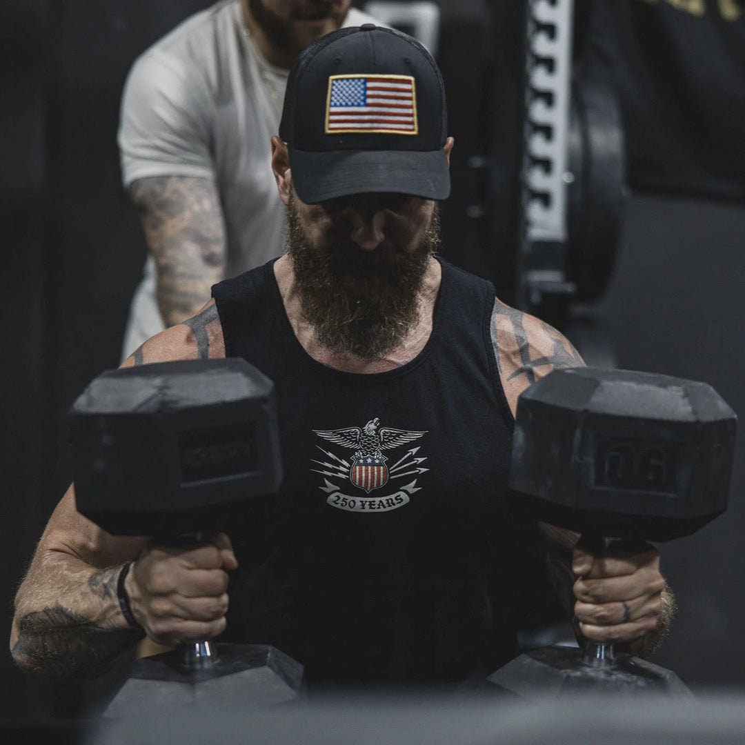 Man lifting dumbbells wearing a black cap with an American flag and the GBRS Group Lead and Lace Tank.