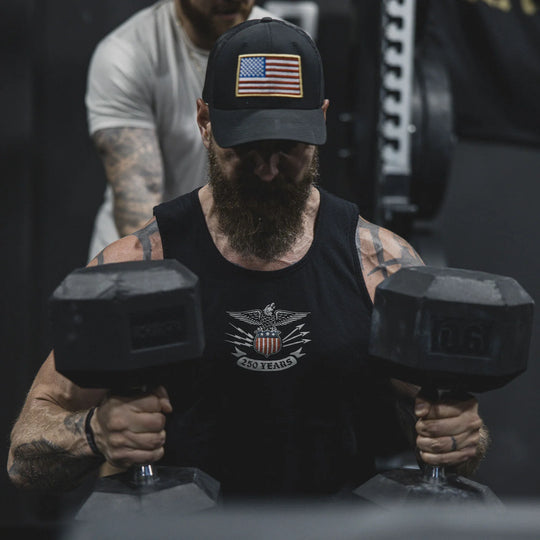 Man lifting dumbbells wearing a black cap with an American flag and the GBRS Group Lead and Lace Tank.