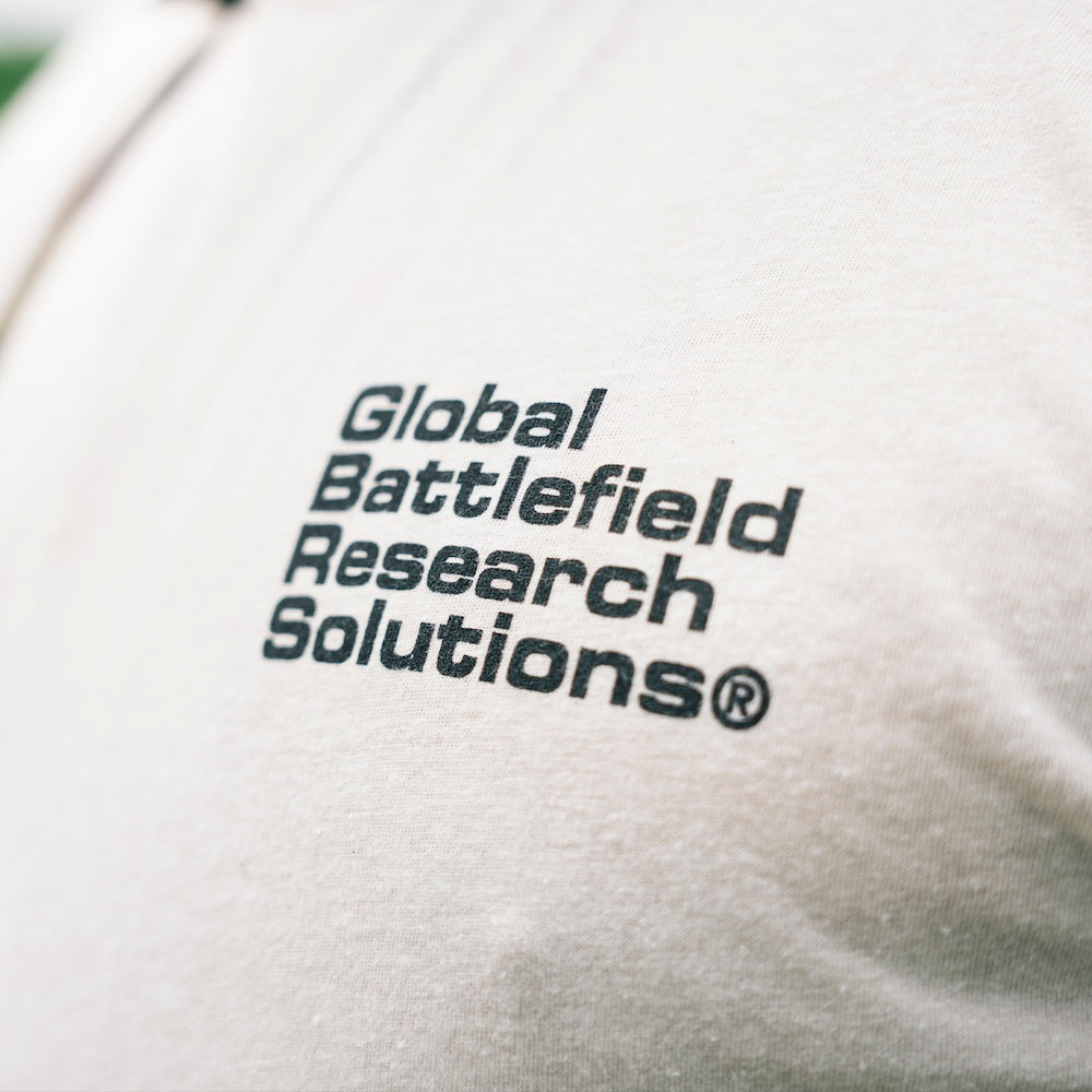 Close-up of the cream GBRS Group Obscured Short Sleeve Shirt design with black-printed text reading 'Global Battlefield Research Solutions'.