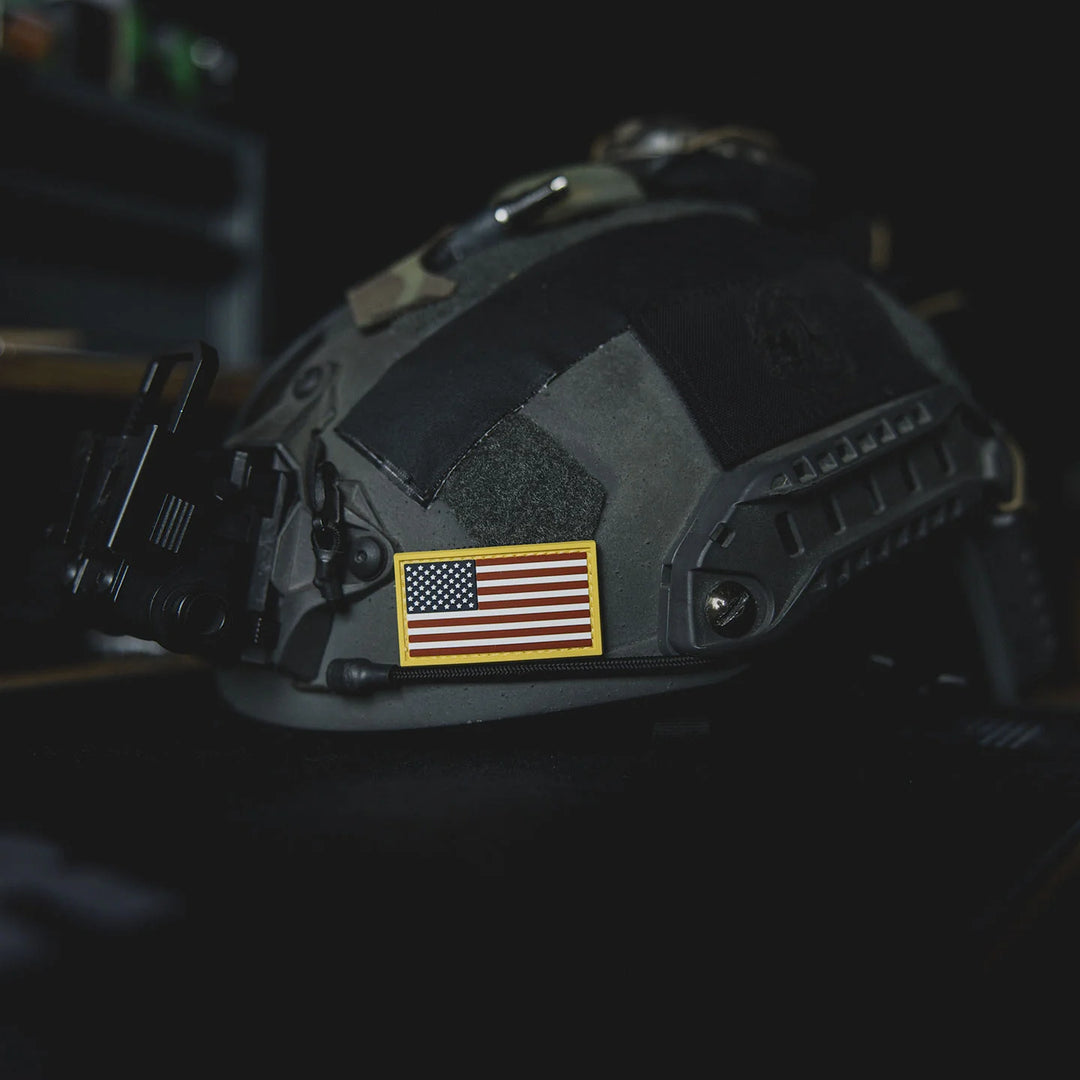 Black tactical helmet with an American flag patch, the GBRS Group Patriotism Front and Center Patch, resting on a table in a dark room.