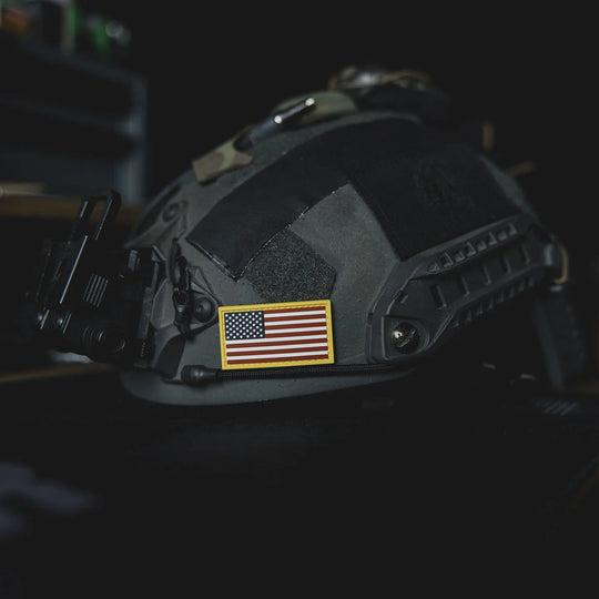 Black tactical helmet with an American flag patch, the GBRS Group Patriotism Front and Center Patch, resting on a table in a dark room.