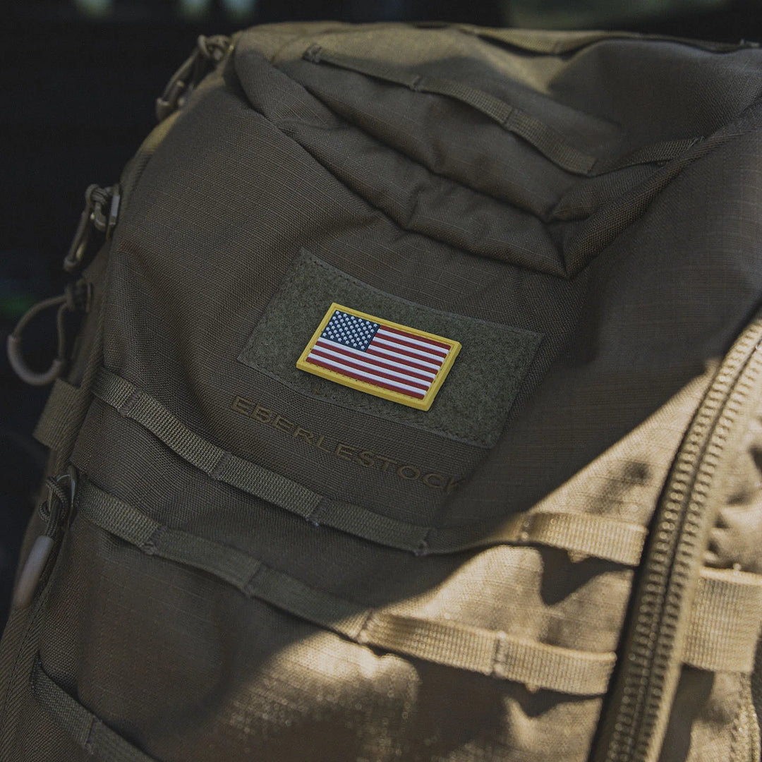 Tactical backpack with an American flag patch, the GBRS Group Patriotism Front and Center Patch, in an outdoors setting.