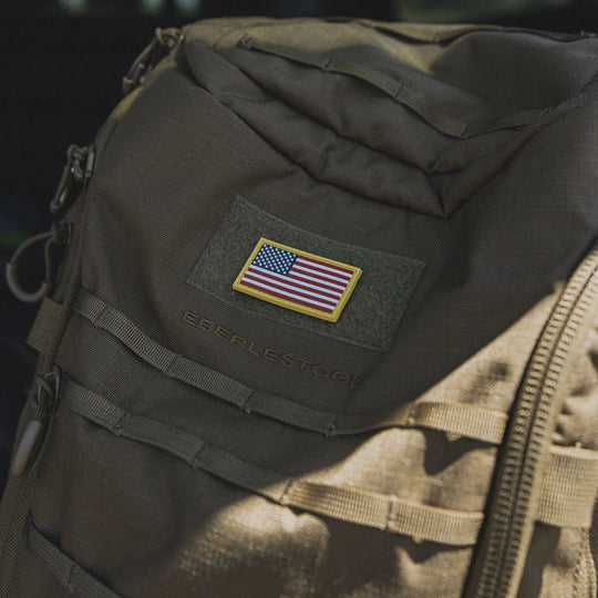 Tactical backpack with an American flag patch, the GBRS Group Patriotism Front and Center Patch, in an outdoors setting.