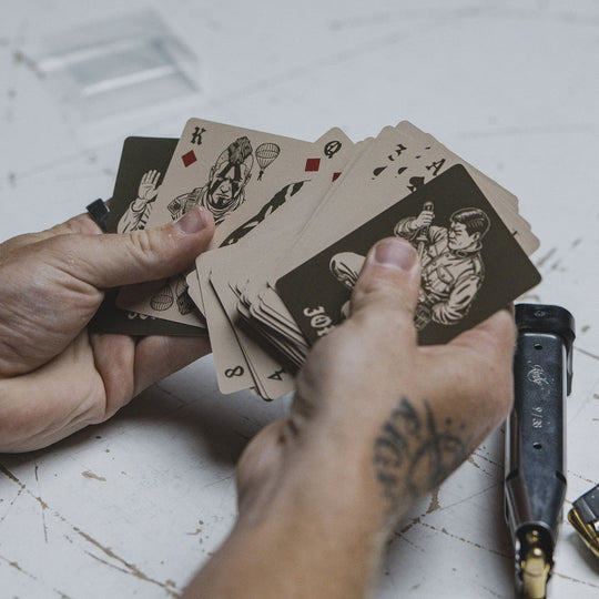 Person holding GBRS Group Patriotism Isn't Dead designed Playing Cards with a tattooed hand on a white table.
