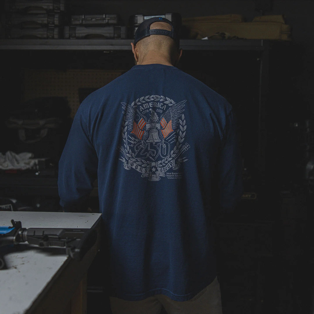 Person wearing GBRS Group Semper Fortis Long Sleeve Shirt with a design on the back, in a workshop setting.