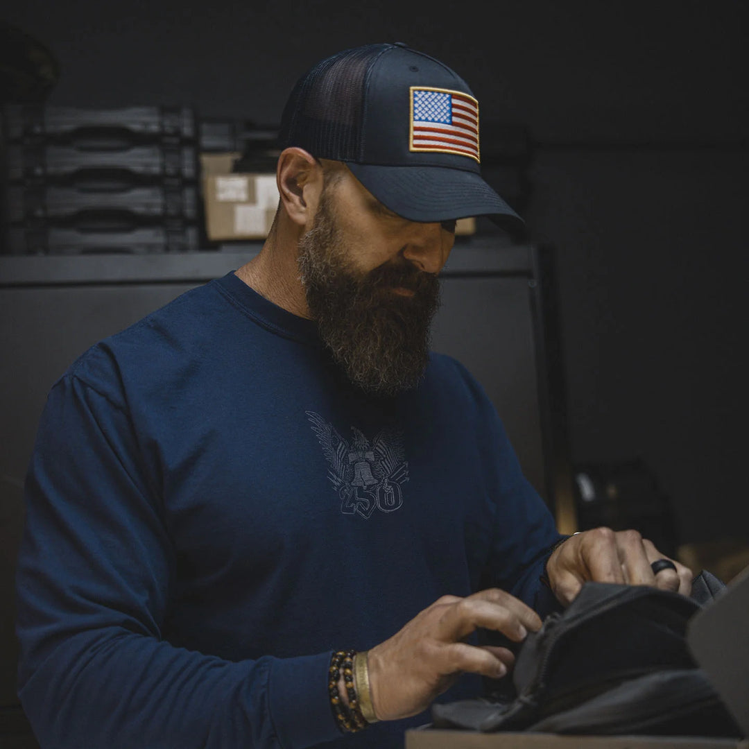 Man wearing a blue cap with an American flag patch and the GBRS Group Semper Fortis Long Sleeve Shirt, working with his hands.