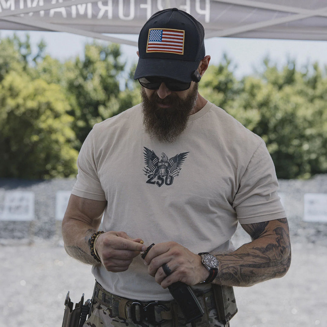 Man wearing a cap with an American flag, sunglasses, and the GBRS Group Semper Fortis Short Sleeve Shirt while standing under a tent outdoors.