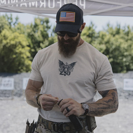 Man wearing a cap with an American flag, sunglasses, and the GBRS Group Semper Fortis Short Sleeve Shirt while standing under a tent outdoors.