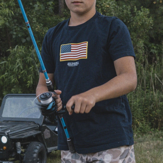 Child wearing the GBRS Group Navy Blue Youth Front & Center Short Sleeve Shirt, holding a fishing rod outdoors.