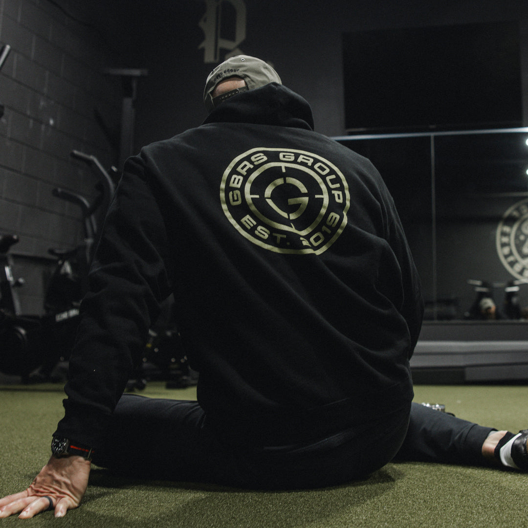 GBRS Group Instructor Pullover Hoodie, pictured in black in a gym lifestyle setting showing the backprint design