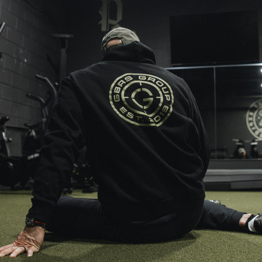 GBRS Group Instructor Pullover Hoodie, pictured in black in a gym lifestyle setting showing the backprint design