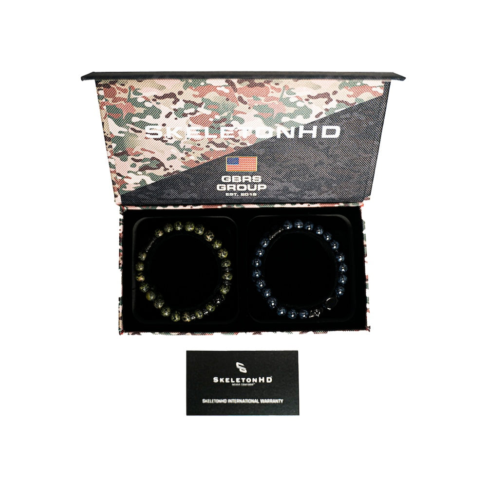 An open camouflage-patterned gift box containing two beaded bracelets on a black insert, with a small black SkeletonHD warranty card below. The box lid shows the brand name and 'Made in USA' text.