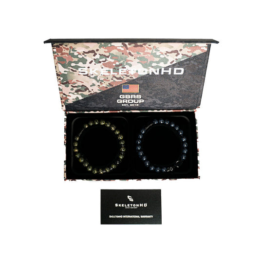 An open camouflage-patterned gift box containing two beaded bracelets on a black insert, with a small black SkeletonHD warranty card below. The box lid shows the brand name and 'Made in USA' text.